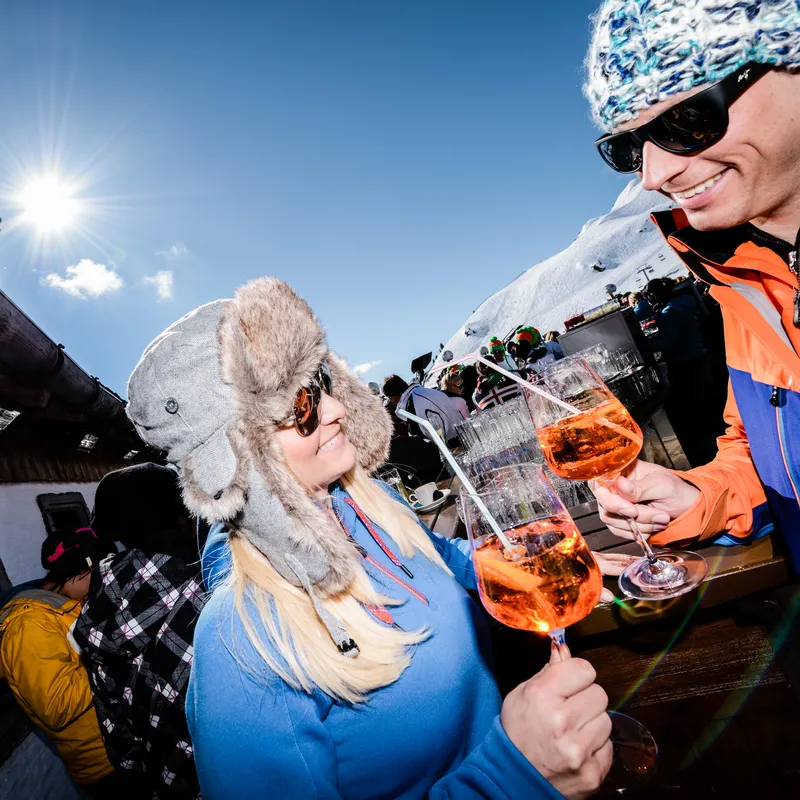 Paar trinkt Aperol Spritz bei Sonnenschein auf einer Skihütte in den Alpen